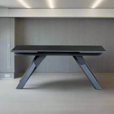 Modern black dining table with unique legs against a neutral wall.